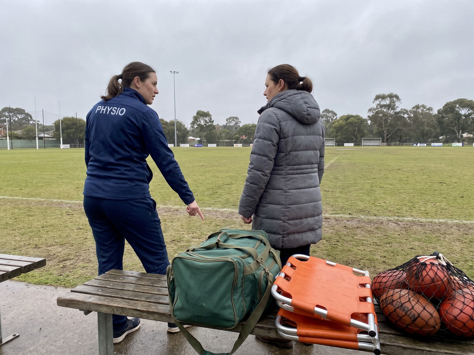 A club physio talking to a mother beside the players' bench at a junior football ground
