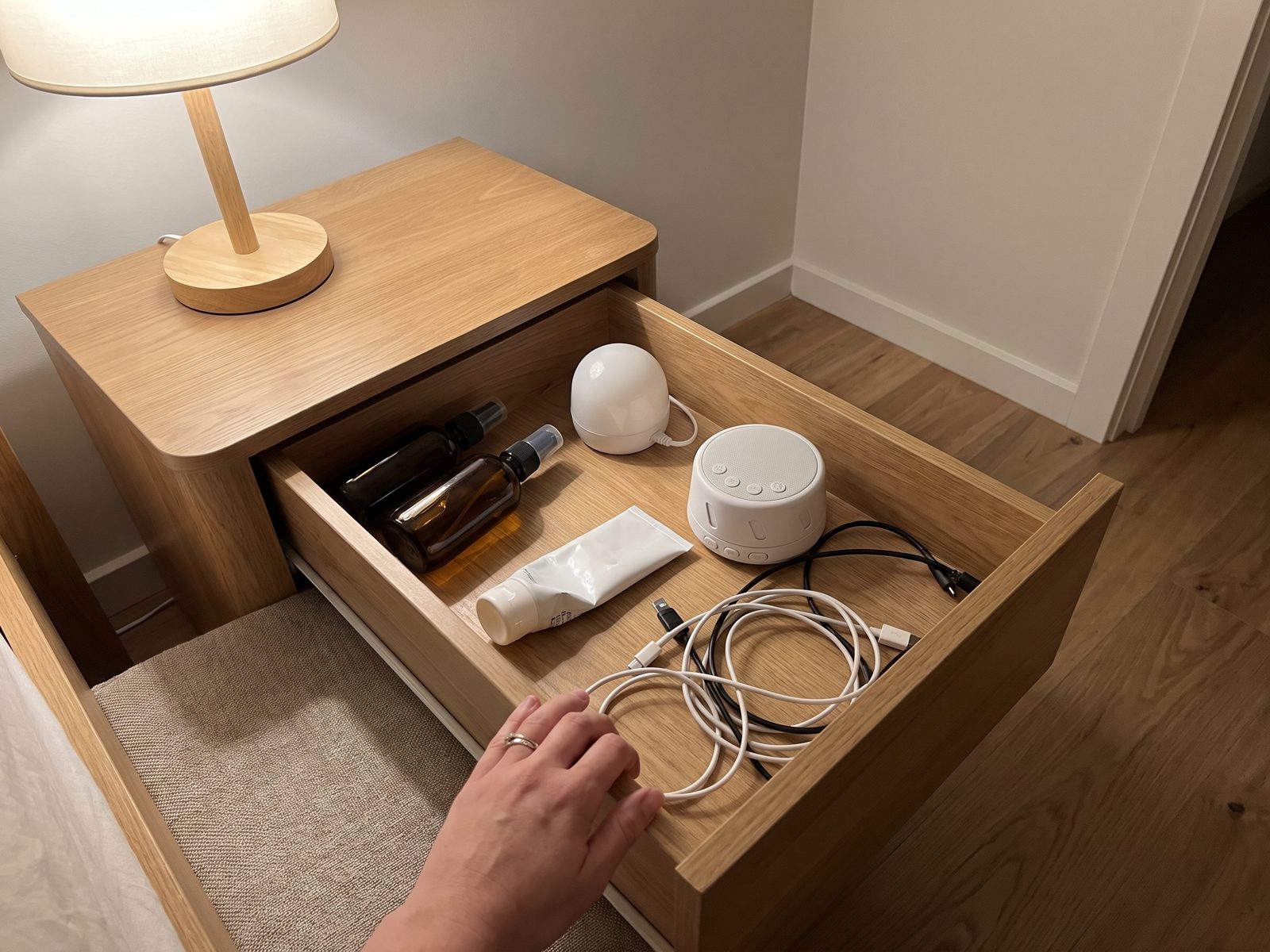 A bedside drawer pulled open, full of sleep gear that did not work - spray bottles, a night light, a white noise machine and tangled cables