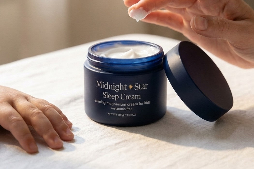 Midnight & Star Sleep Cream open on a bed, a parent&rsquo;s hand and a child&rsquo;s hand beside it